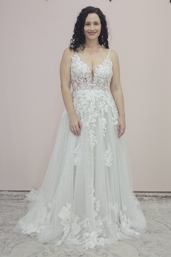 This romantic A-line wedding dress features an illusion V-neck bodice adorned with smattered floral lace and delicate silver beading for a soft shimmer. The full beaded and sequinned underskirt adds a touch of glamour beneath the flowing silhouette